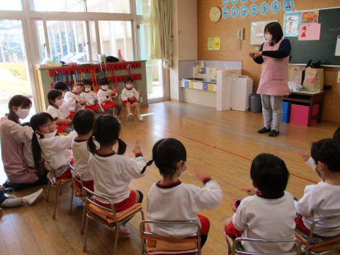 保育士と園児達、手を挙げて遊ぶ。6月【年少々】スタンプ遊び、幼稚園の教室風景。