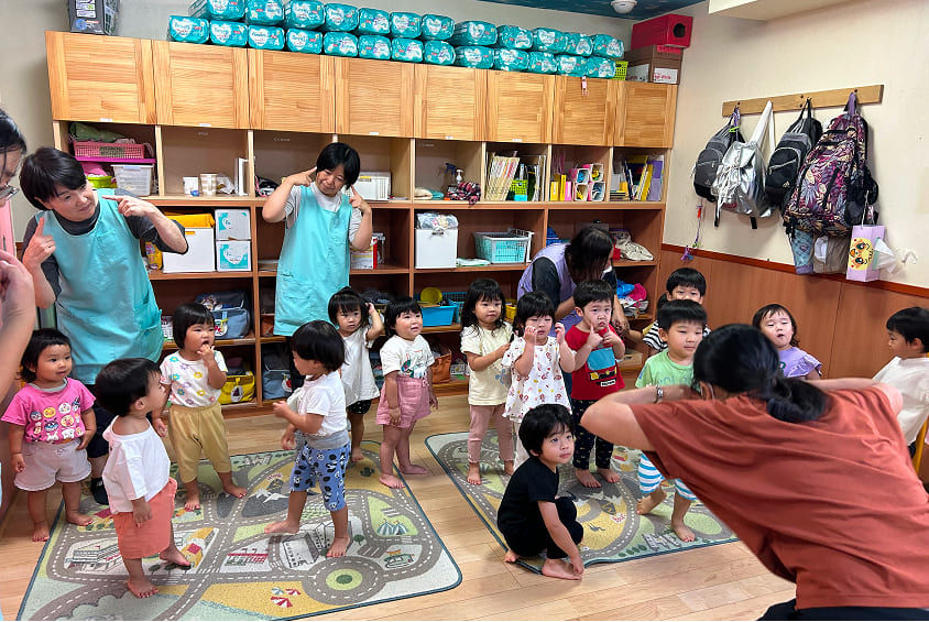 保育士と子供たちが踊っている様子。楽しそうな子供達、笑顔いっぱい。日野ルーム、マジオブルームキッズ。