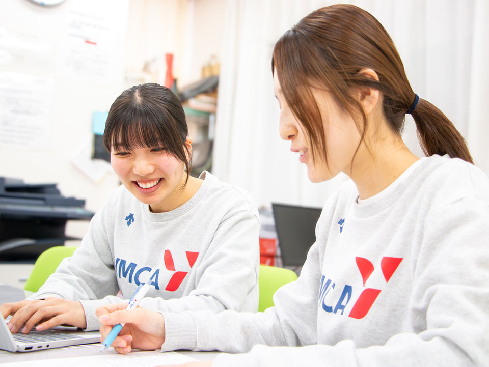 YMCAのスウェットを着た女性2人がPCで共同作業