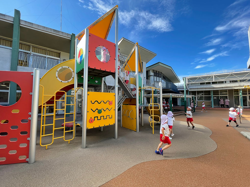 園庭で遊ぶ子供たち。カラフルな遊具と園舎、晴天の下で笑顔が輝いています。