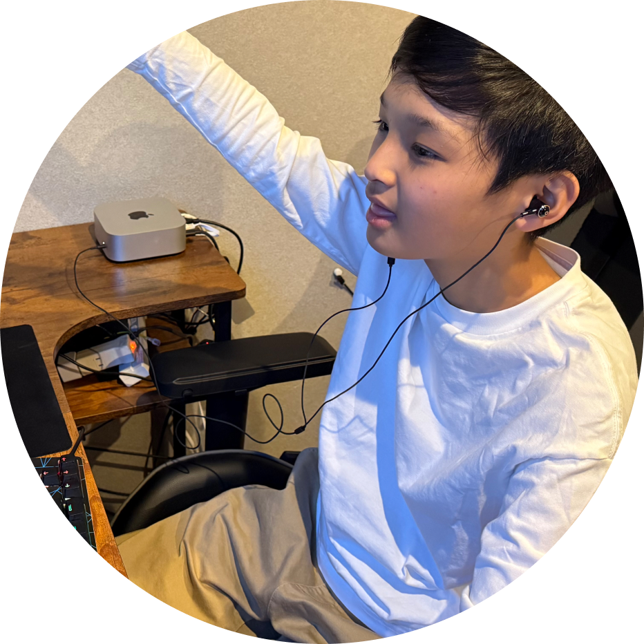 イヤホンをして机で手を挙げる少年