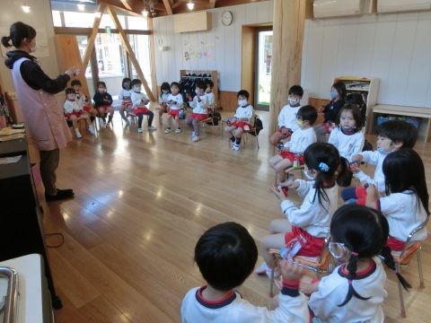 保育士と園児たち、教室にて。子ども達が座り、話を聞いています。 ７月のお誕生日会。