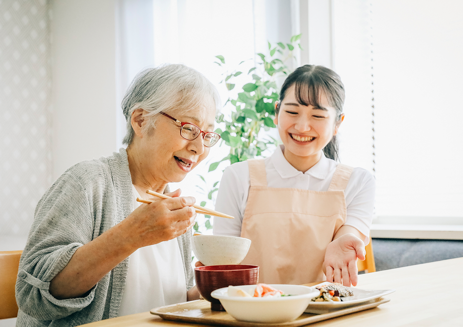 食事を介助するスタッフと笑顔で食事を楽しむ高齢女性