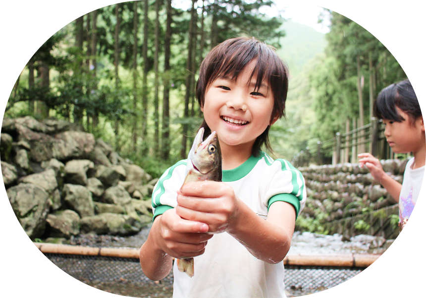 笑顔の男の子が魚を持って、屋外で微笑んでいます。緑豊かな背景の中で家族と楽しむ