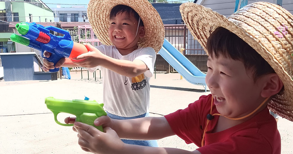 笑顔で水鉄砲をする子供たち。夏の日、水遊びの様子。めぐみ幼稚園。
