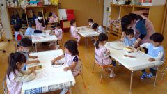保育園の様子。子供達がテーブルで絵を描いている。1月【年長】今週の様子。先生もいます。