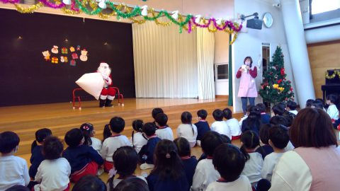 サンタクロースがステージでプレゼントを配る様子。12月【年少】　クリスマス会、子供達が見ています。