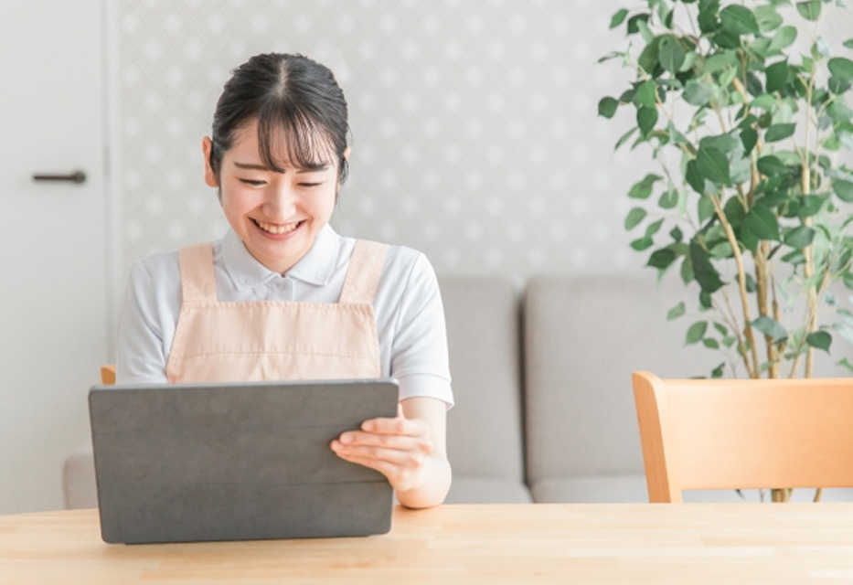 タブレット端末で作業をしながら笑顔を見せる保育士の女性