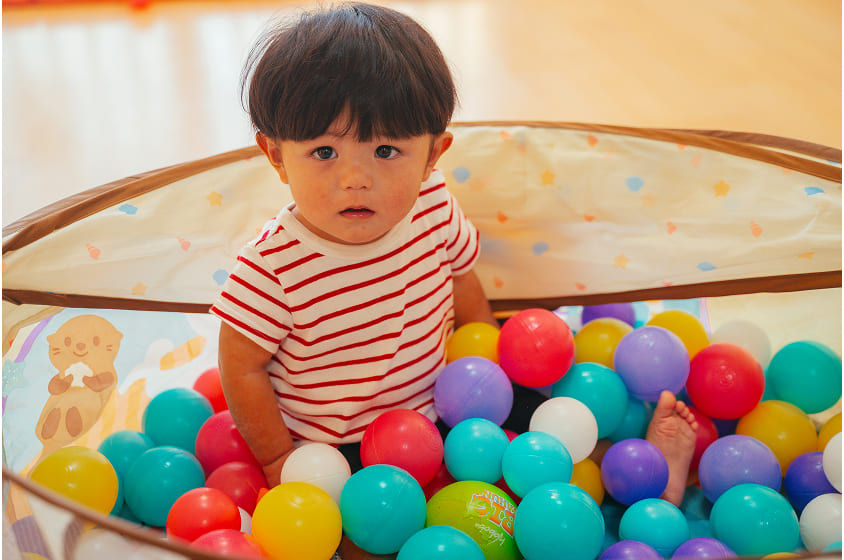 ボールプールで遊ぶ男の子、赤いボーダーシャツ。カラフルなボール、楽しそう。