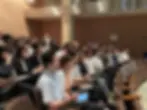 講堂で真剣に講演を聞く多くの参加者、学習に集中している様子。