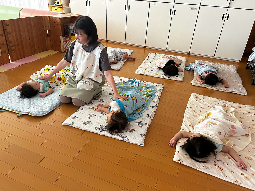 お昼寝を見守る保育士と布団で眠る園児たち