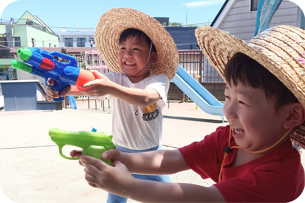 二人の子供たちが水鉄砲で遊んでいます。笑顔で夏の幼稚園の行事を楽しんでいます めぐみ幼稚園