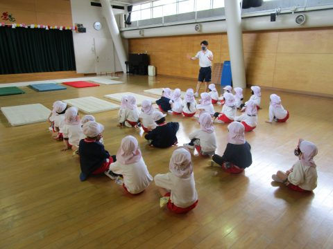 先生と子供たち、園児達が座って話を聞いています。年長組　参観日、保育園の様子。