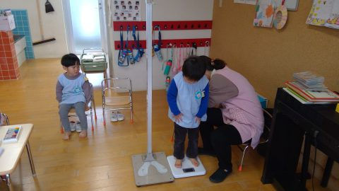 保育園で体重測定をする子供たち。計測中、もう一人の子供が待機しています。7月【年少々】今週の様子
