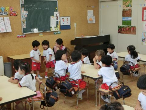 保育園の教室で、先生と子供たちが話しています。黒板に文字が書いています。７月のお誕生日会
