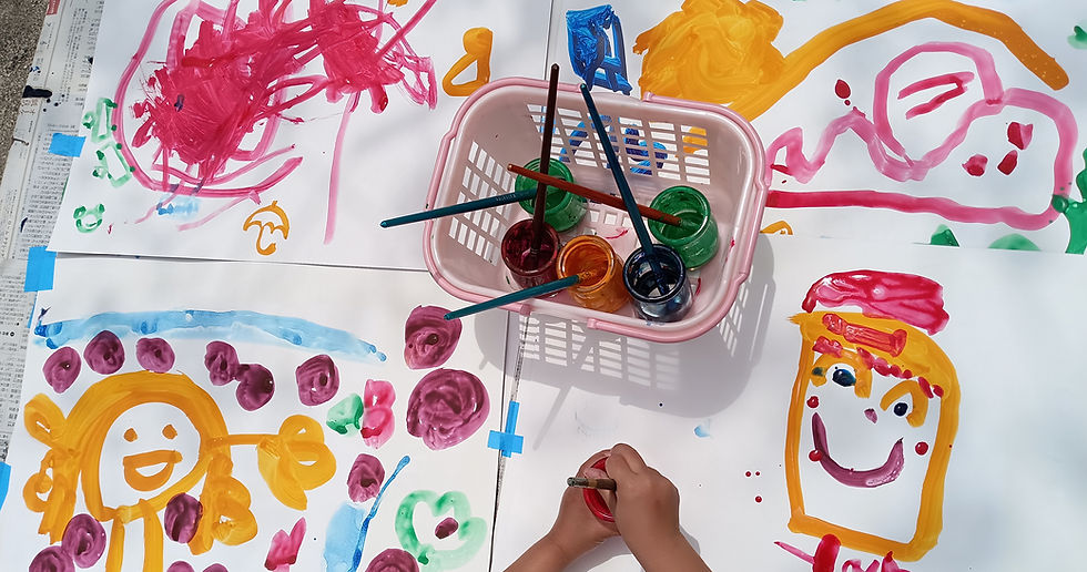 絵の具と筆、バスケットに入った絵筆と、子供が絵を描いています。めぐみ幼稚園