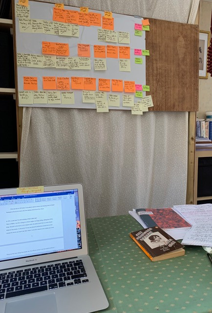 laptop on desk with board full of post-its planning novel