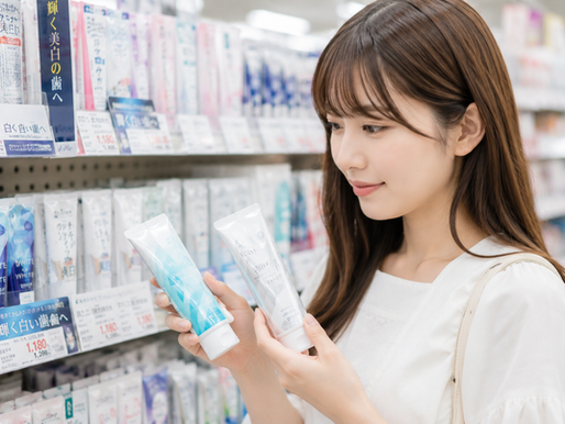 ドラッグストアで若い女性が歯磨き粉2本を手に取り、棚の「輝く白い歯へ」や価格表示を見比べている