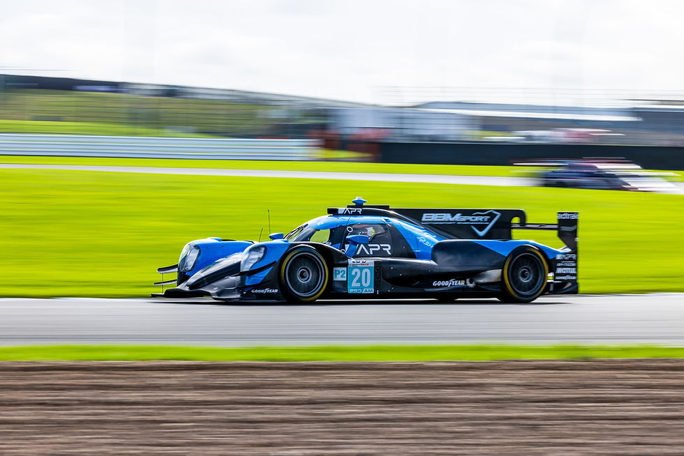 Blue-and-black race car No.20 with APR and BBM Sport logos speeds on a track, background blurred.