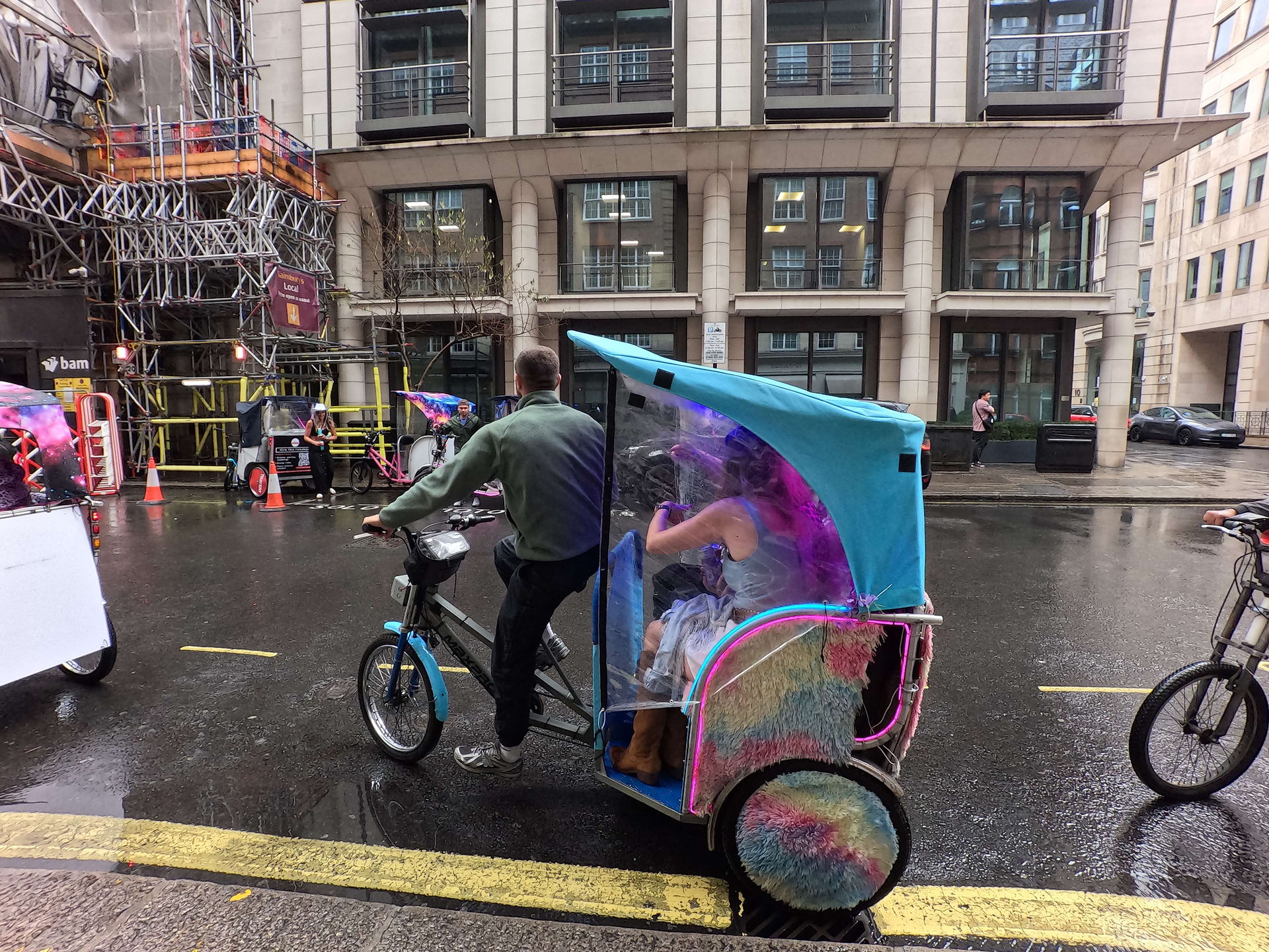 Professional rickshaw driver operating a branded pedicab in the rain in London.