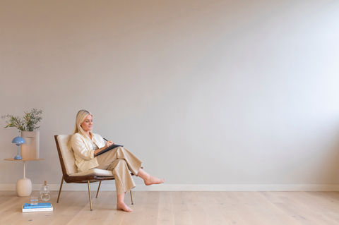 Ung dame sitter i designerstol og arbeider, hun er barføtt og komfortabel med varme i gulvet fra Varmecomfort.