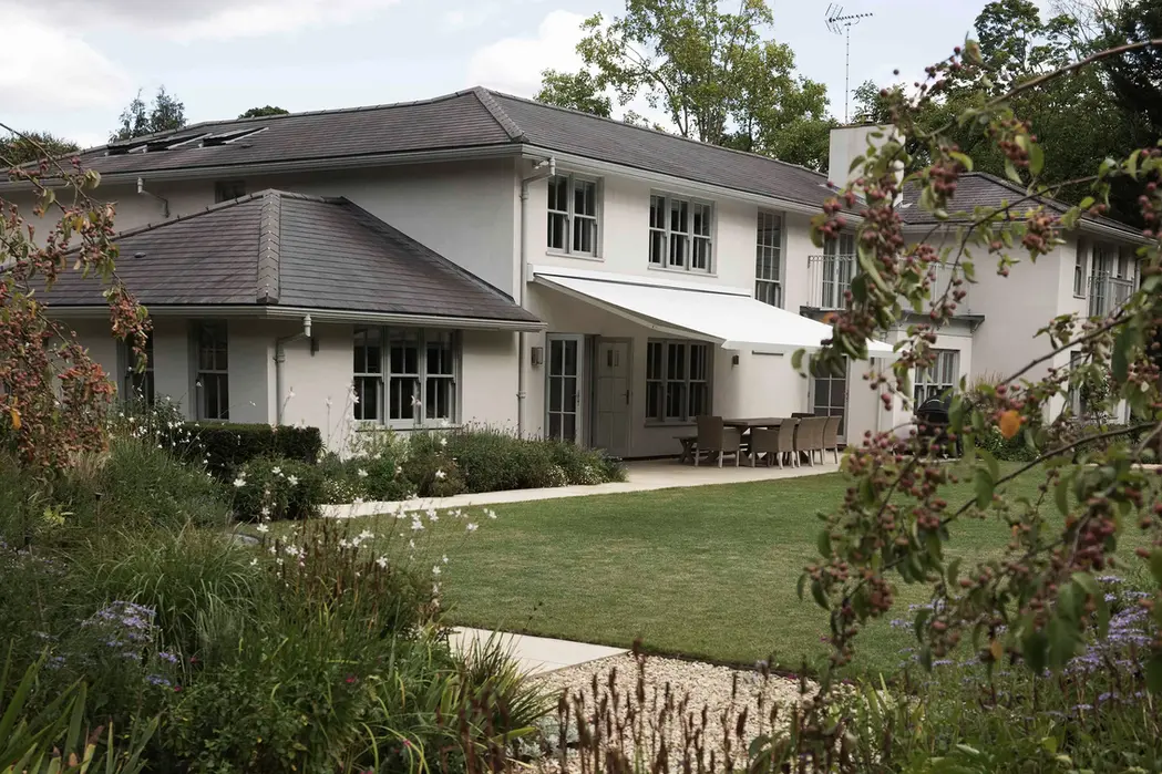Rendered house with a hipped tiled roof and single-storey wing, retractable awning over a dining terrace and lawn.