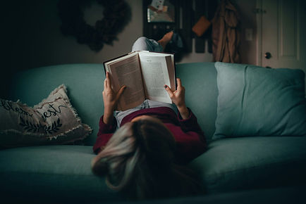 A teenage girl, sitting on the sofa, reading a book.