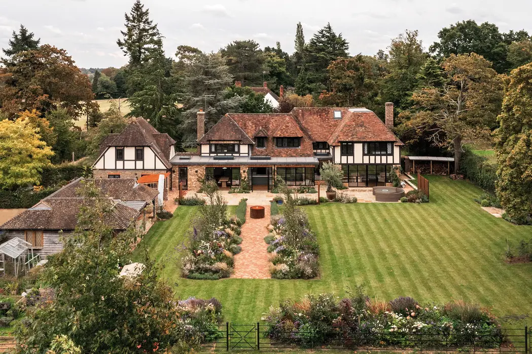 Timber-framed house with a new brick and glass rear extension, flat roof and full-height black-framed glazing onto a terrace and garden.