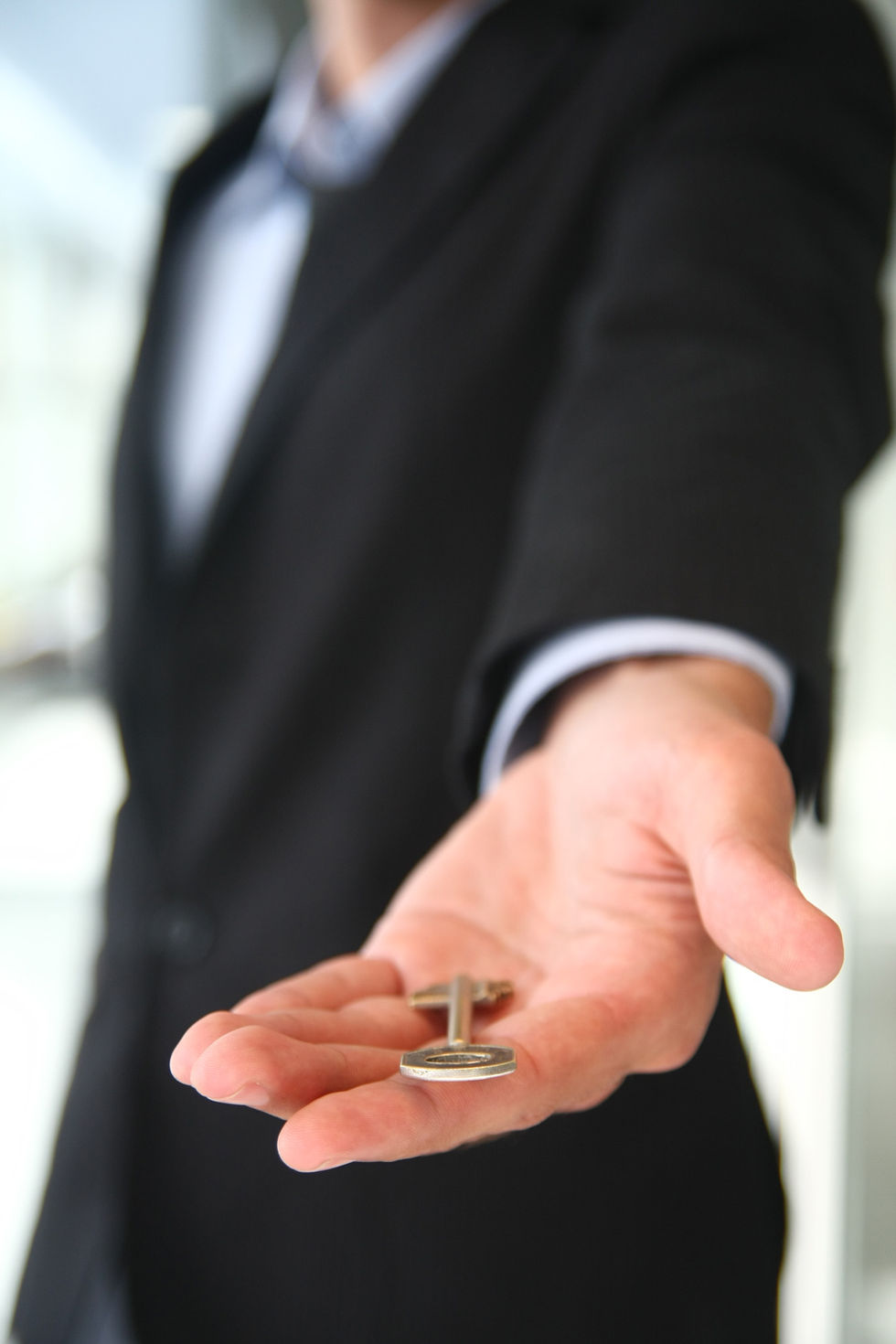 Man's hand holding a cufflink accessory in front of blurred background