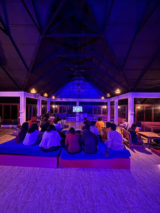 Backpackers enjoying a cozy movie night in the common lounge, surrounded by warm lighting and comfy seating.