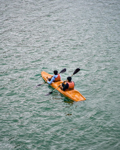 Kayakers gliding through tranquil water at Ponmudi Dam, flanked by lush tropical forest and rocky banks.