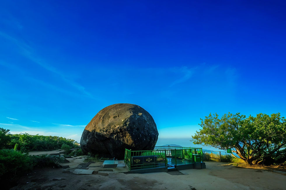Large rock under clear blue sky, flanked by green trees and a fenced platform. Peaceful outdoor setting, bright and serene ambiance.
