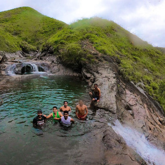 Natural infinity pool at Zostel Vagamon, nestled among lush green hills, offering panoramic views of mist-covered mountains under a cloudy sky.