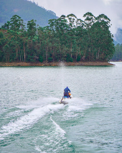 Young travelers paddling a rowboat across the calm waters of Ponmudi Dam, green forested hills reflected in the reservoir.