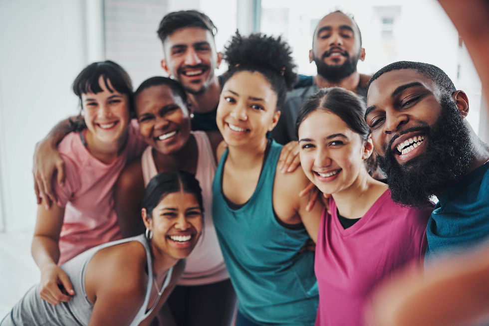 Smiling diverse group of friends crowd into a bright indoor selfie, arms around each other, wearing colorful tops.