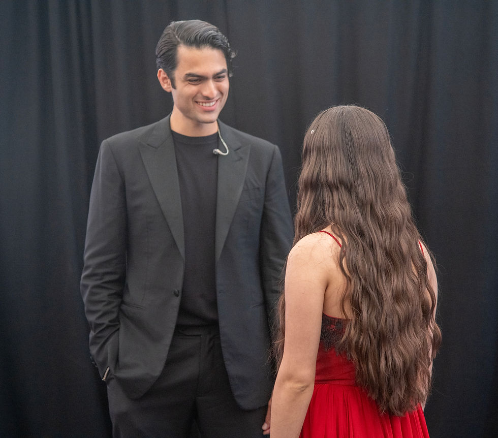 Matteo Bocelli in a black suit interacts with Joaquina, who is dressed in a red outfit, backstage at Hyde Park before the concert.