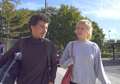 Two UAL students walking together on campus, carrying bags and equipment.
