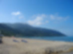 A digital compact camera photo of a tranquil beach with empty lounge chairs, calm turquoise waters, and a mountainous landscape in the background, illustrating the serene and nostalgic qualities of digital camera photography