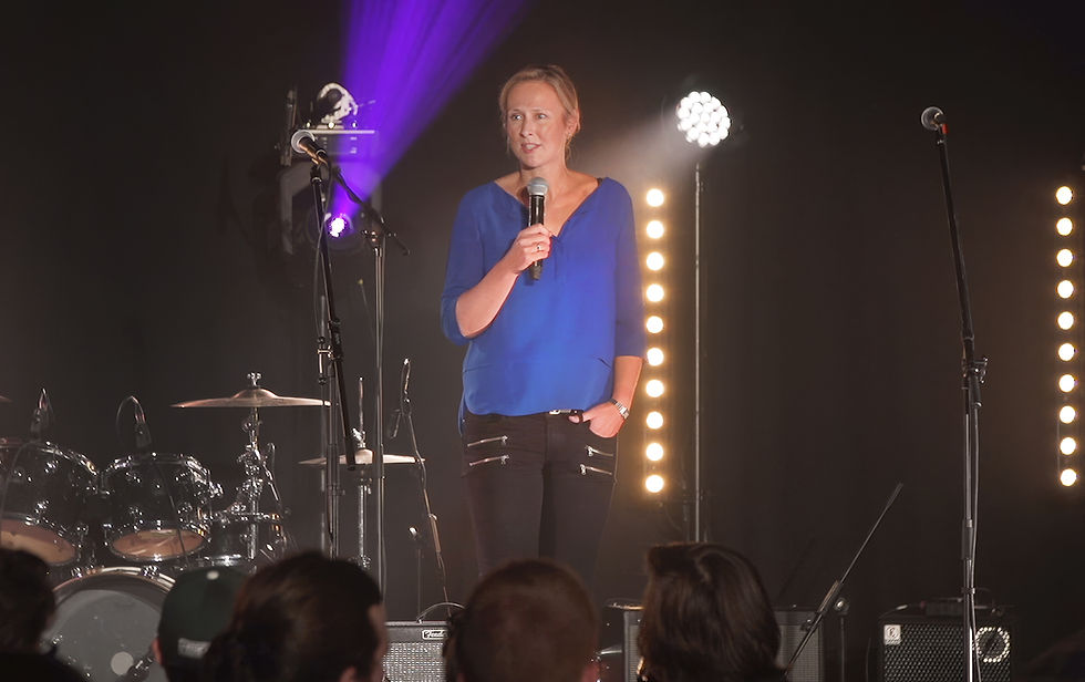 Speaker holding a microphone on stage under event lighting, filmed during a live event to showcase event videography.