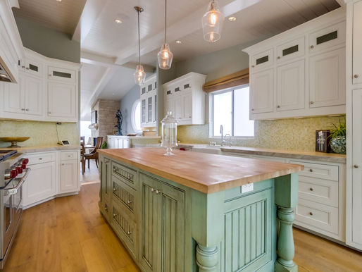 updated modern kitchen with white cabinets, yellow backsplash, and green island with wooden countertops