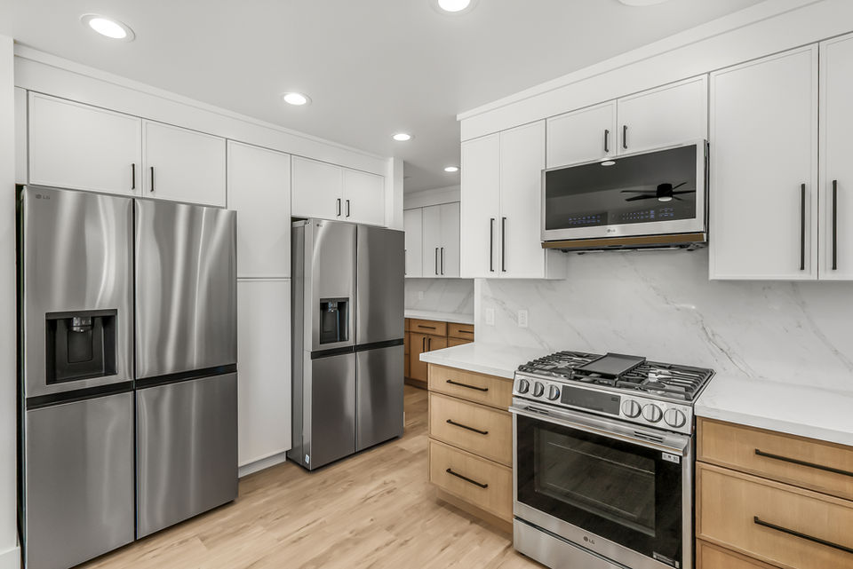 Kitchen view with double fridges and remodeled stove top with hanging cabinets and vent stove.