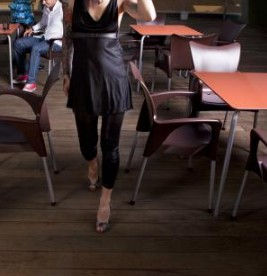 Miniatura: Mujer en vestido oscuro y tacones camina junto a mesas de café.