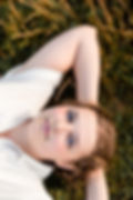 Op deze foto staat Lisa die in het gras ligt. Ze heeft een rustige energie en in haar blauwe ogen een bereidheid en vastberadenheid om jouw te helpen als hoogsensitieve vrouw.