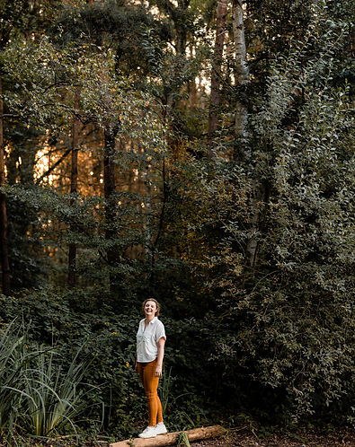 Lisa De Grave, de HSP-coach naar verbinding die poseert op een boomstam bij zonopgang in het bos waar sessies doorgaan.