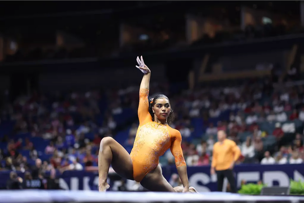Gymnast eMjae Frazier of the Florida Gators, performing her routine, on the floor, with one arm raised above her head.
