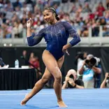 Gymnast Jordan Chiles in the middle of her floor routine, one arm on her hip and the other up by her face.
