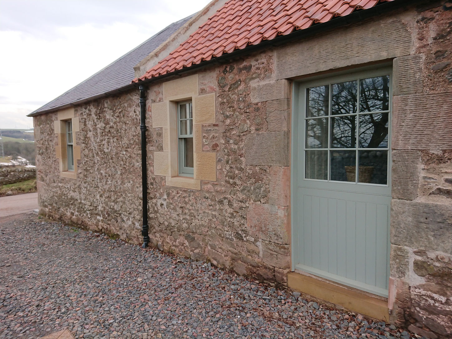 Stone cottage with red roof, green door, and gravel