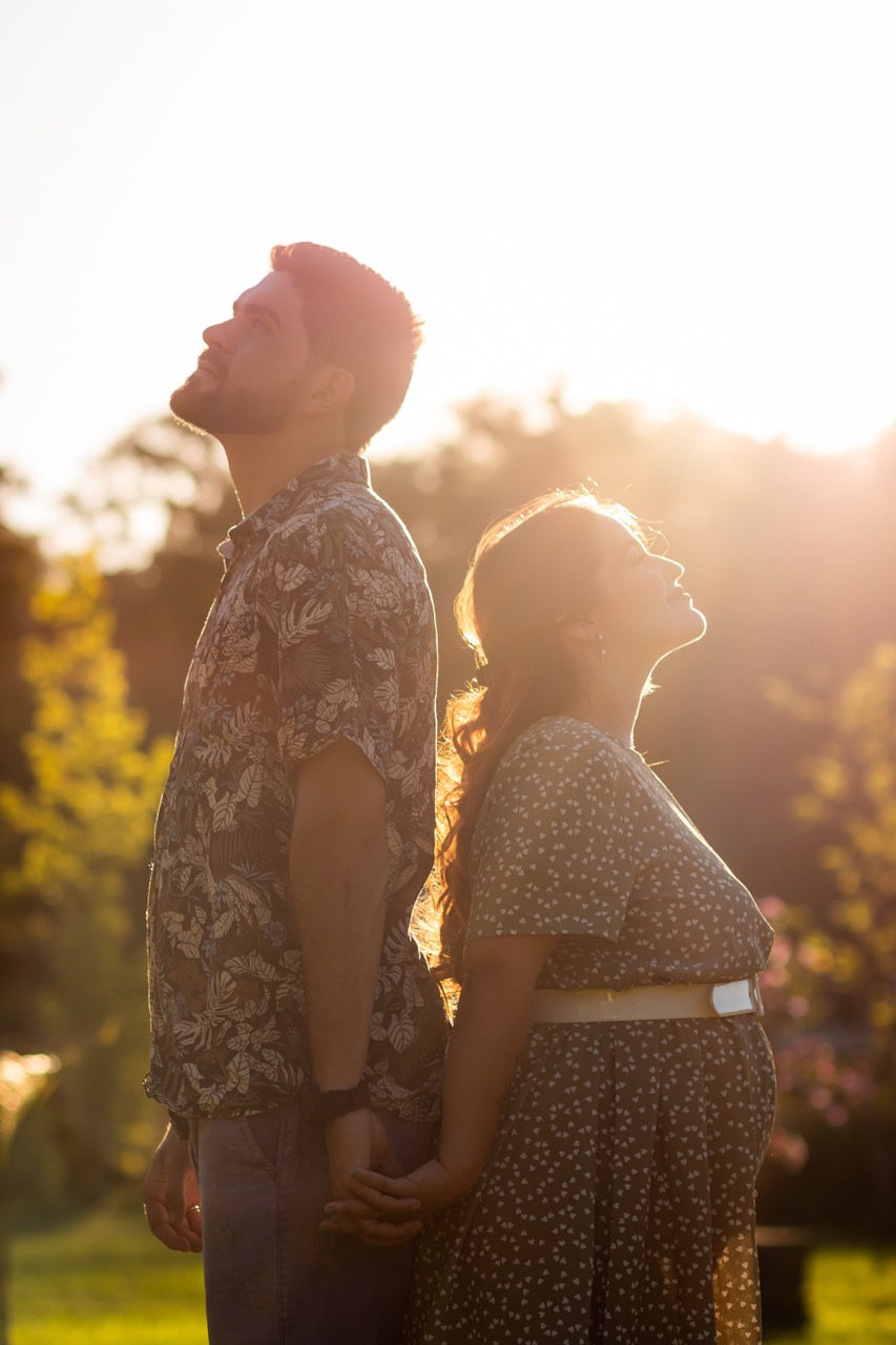 Couple standing back-to-back in sunlight, outdoors.