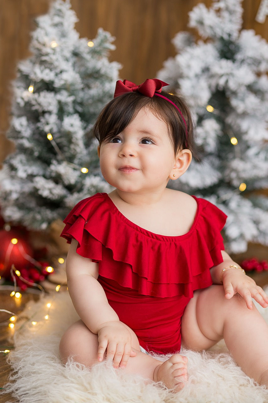 Child in red outfit, sitting near decorated trees.