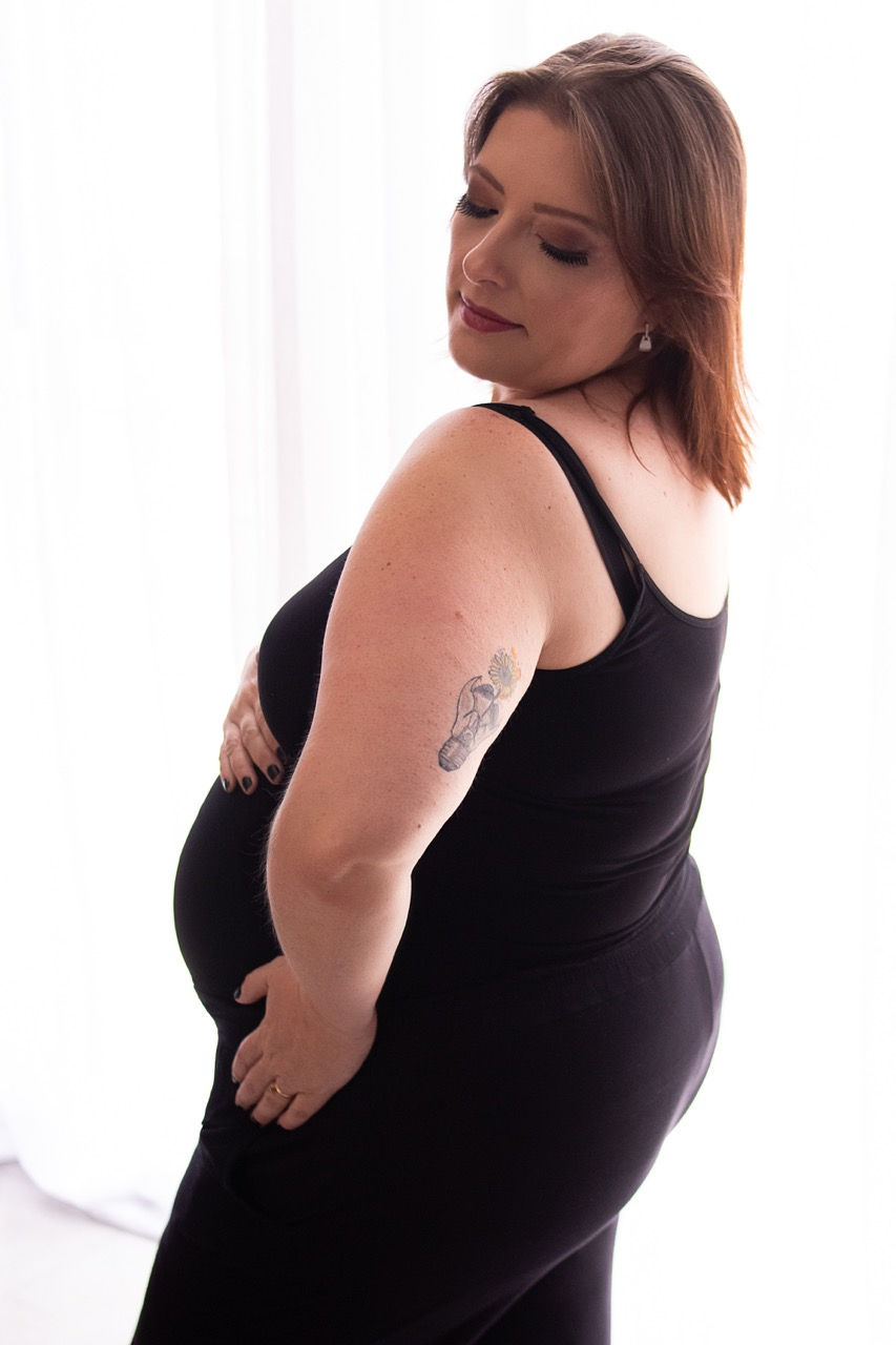 Pregnant woman in black dress, gently holding belly.